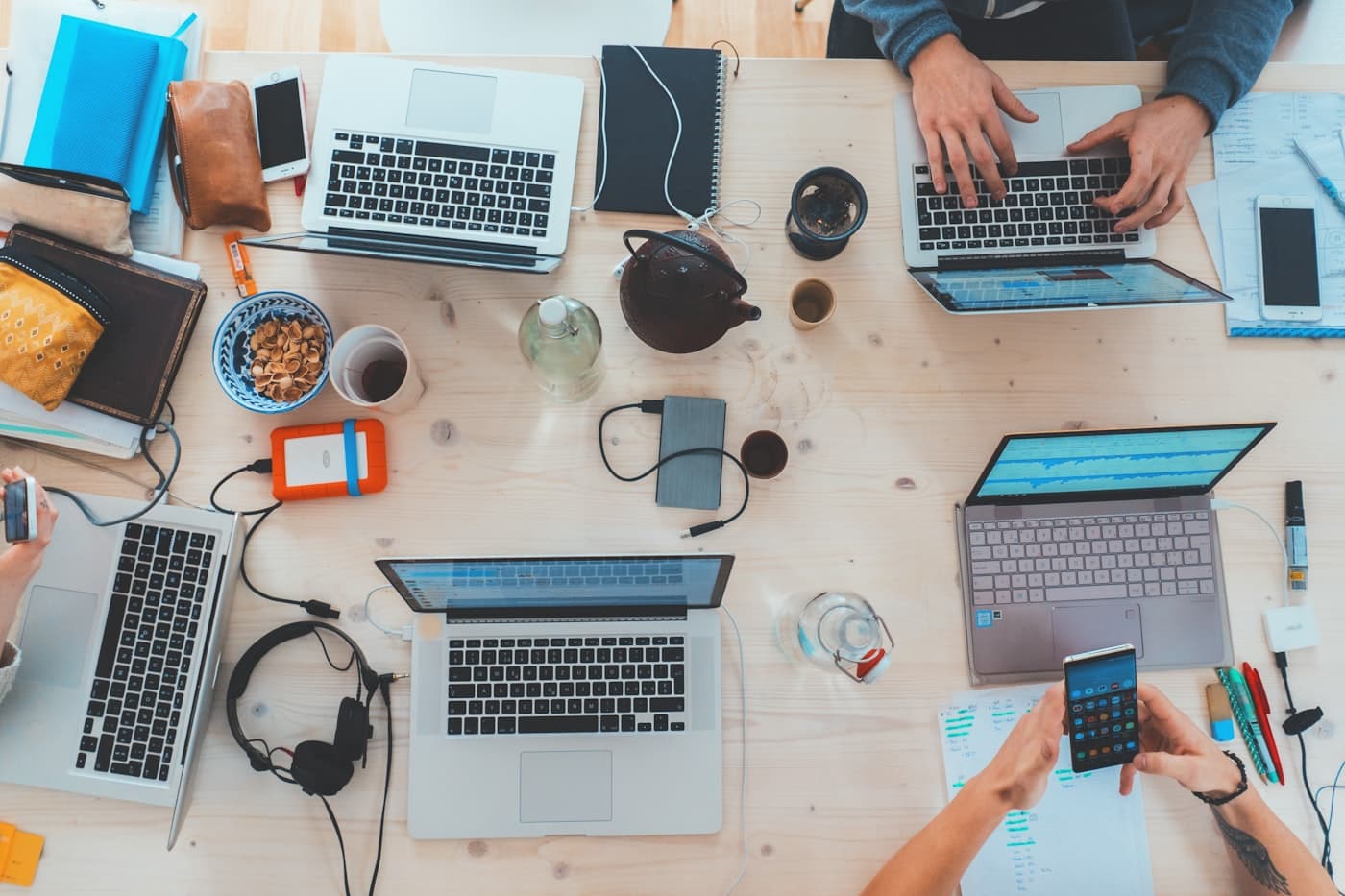 A shared worktable with laptops, a phone, notebooks, and testing devices